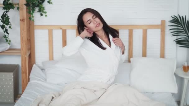 Mujer joven se despertó por la mañana, estirada en la cama, sonríe, disfruta de la mañana — Vídeo de stock