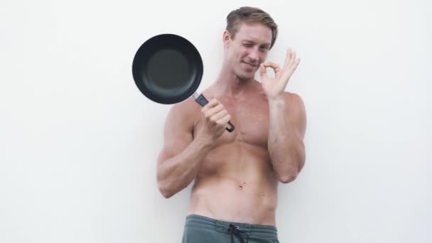 Сексуальний чоловік без сорочки зі сковородою, посміхається, показує знак ок, фліртує на камеру — стокове відео