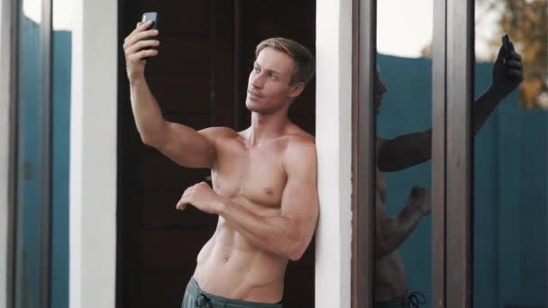 Shirtless man with muscular body makes selfie on phone, shows tongue, funny face — Stock Video