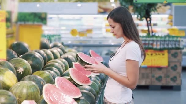 Jonge toeristische vrouw kiest de helft van de watermeloen in de supermarkt, snuift, neemt het — Stockvideo