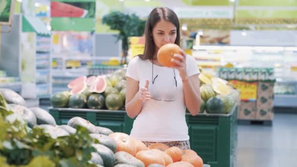 若い観光客の女性は、食料品店でカボチャを選択します,スニッフとそれを取る — ストック動画