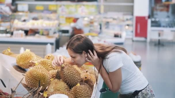 Genç turist kadın markette olgun meyveleri seçiyor, kokluyor ve bir tane alıyor. — Stok video