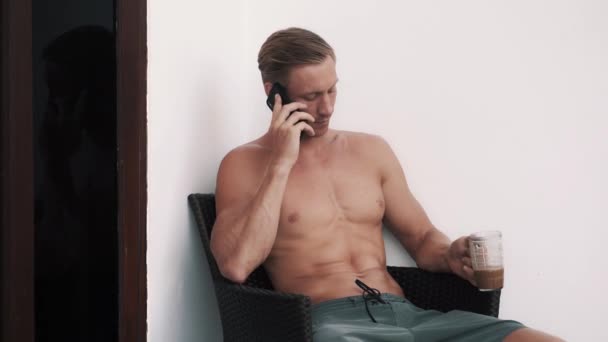 Shirtless sexy man sitting in armchair outdoor, talking on phone and laughing — Stockvideo