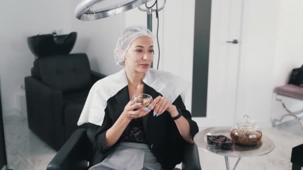 Giovane donna sulla procedura di cura dei capelli nel salone di bellezza, beve il tè e si rilassa — Video Stock