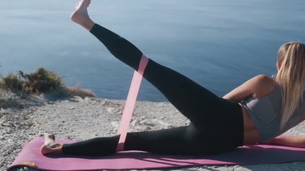 Menina se deita no tapete e faz exercícios com elásticos, treina suas nádegas, corpo — Vídeo de Stock