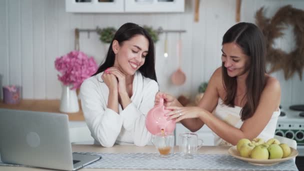 Két gyönyörű nő teát iszik a konyhában reggel és beszélgetnek, reggeli idő. — Stock videók