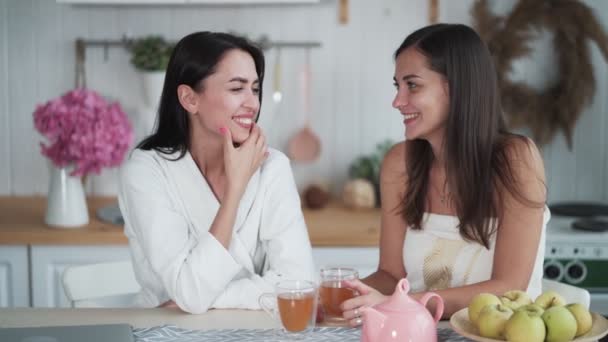 Two beautiful woman drink tea at kitchen in morning and talk, breakfast time — ストック動画