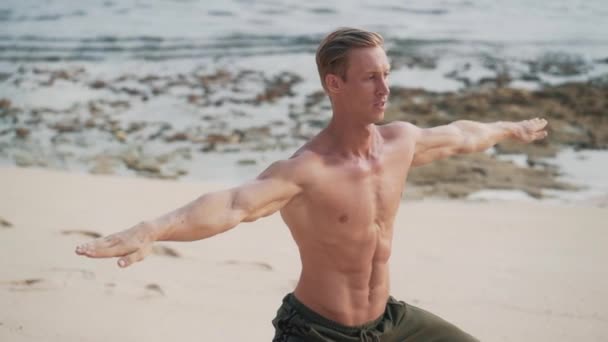 Uomo con corpo muscolare che fa esercizi di yoga sulla spiaggia al tramonto, rallentatore . — Video Stock