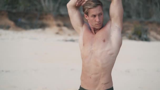 Férfi izmos test csinál streching gyakorlatok a strandon naplementekor, lassított felvétel. — Stock videók