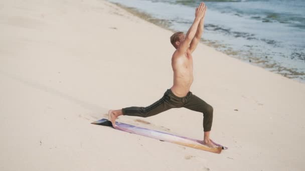 Homem com corpo muscular fazendo exercícios de ioga na praia ao pôr do sol, câmera lenta . — Vídeo de Stock