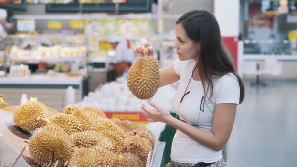 Genç turist kadın markette olgun meyveleri seçiyor, kokluyor ve onlardan birini alıyor. — Stok video