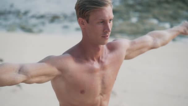 Man med muskulös kropp gör yoga övningar på stranden vid solnedgången, slow motion. — Stockvideo