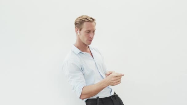 Мужчина в рубашке слушает музыку с беспроводными наушниками, танцами, белым фоном — стоковое видео