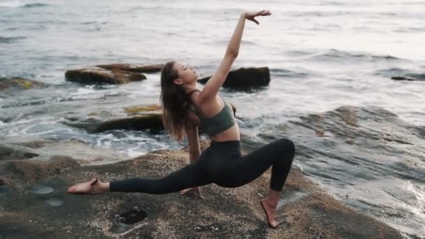 Młoda kobieta robi rozciąganie na plaży, ocean na tle, zwolnione tempo — Wideo stockowe