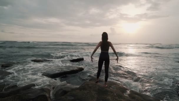 Silueta de chica en la playa del océano extiende sus brazos anchos, puesta de sol en el fondo — Vídeos de Stock