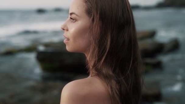 Vista lateral, retrato de mulher olha para o oceano, gentilmente passa a mão sobre o ombro — Vídeo de Stock