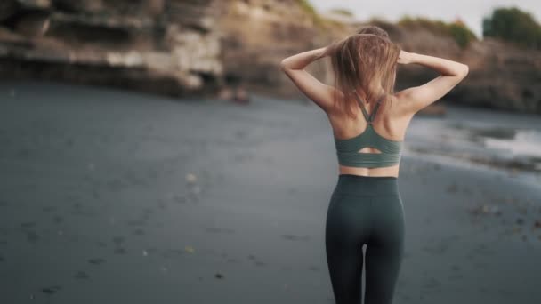 Backside view woman walks at beach, turns around, runs her hand through hair — 비디오