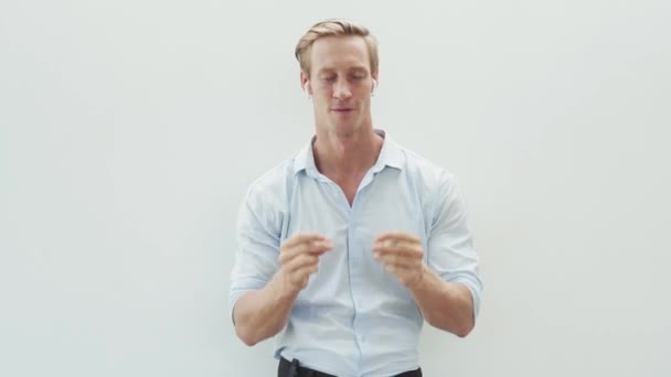 穿着衬衫的男人用无线耳机、跳舞、白色背景听音乐 — 图库视频影像