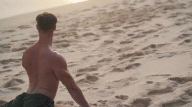 Kaslı vücutlu bir adam gün batımında kumsalda sicim üzerinde çalışır.