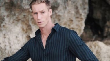 Koyu renk gömlekli yakışıklı bir adam. Kameraya bakıyor ve gülümsüyor.