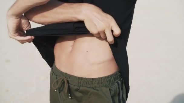 Close-up, torso de homem musculoso tira sua camiseta preta e expõe seus abdominais — Vídeo de Stock