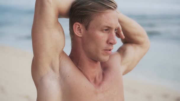 Portret van gespierd blond man doen stretching oefeningen op het strand, slow motion — Stockvideo