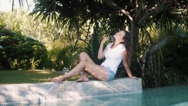 Femme en vêtements d'été décontractés se trouve sur le bord de la piscine, se repose et aime les vacances — Video