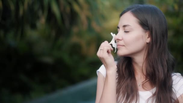 Portrait of woman with frangipani in her hair and hand, sniffs flower and smiles — Stock Video