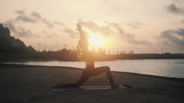 Silhouette of woman practices yoga and doing stretching at sunrise, slow motion — Stock Video