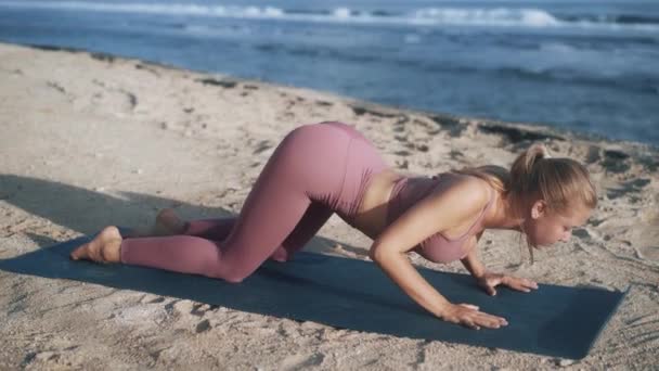 Kadın, okyanus manzaralı, yavaş çekimde, plajda yoga egzersizleri ve esneme hareketleri yapıyor. — Stok video