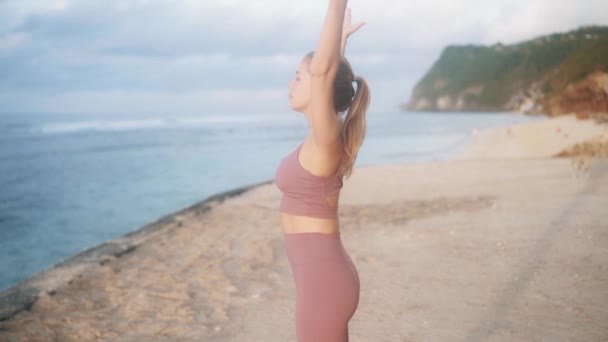 Молодая женщина практикует йогу, упражнения на растяжку на пляже, замедленное движение — стоковое видео