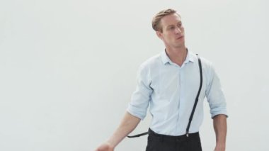 Serious young man in light shirt takes off his suspenders and rolls up sleeves