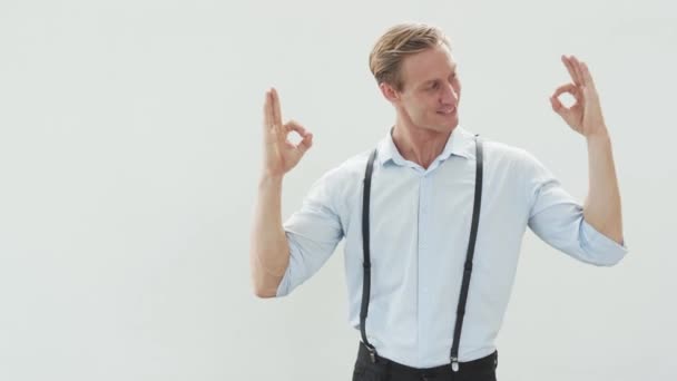 Красивий чоловік у світлій сорочці показує нормальний жест на білому тлі і посмішку — стокове відео