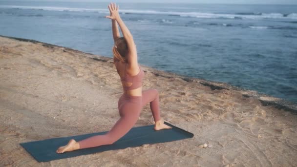 Kvinna gör yoga övningar och sträcker sig på morgonen på matta på stranden, slow motion — Stockvideo