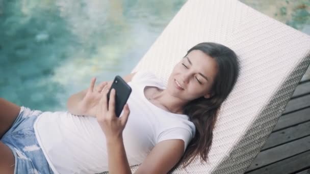 Γυναίκα ελεύθερος επαγγελματίας βρίσκεται σε ξαπλώστρα κοντά στην πισίνα και χρησιμοποιεί το τηλέφωνο για την εργασία, πληκτρολογεί το μήνυμα — Αρχείο Βίντεο