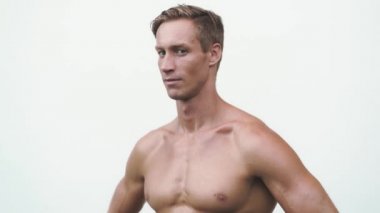 Shirtless man on white background, shows thoughtful emotion on his face then laughs