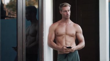 Portrait of sexy muscular shirtless man uses mobile, touches screen with fingers