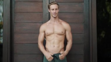 Portrait, shirtless man with muscular body shows sign thumb up, wood background