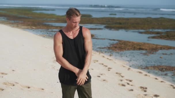 Man with muscular torso poses taking off black vest on bank — Stockvideo