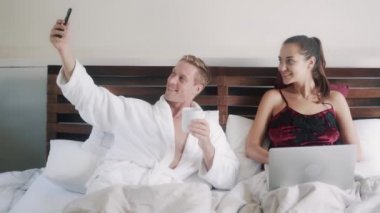 happy young family makes selfie resting in bed in morning