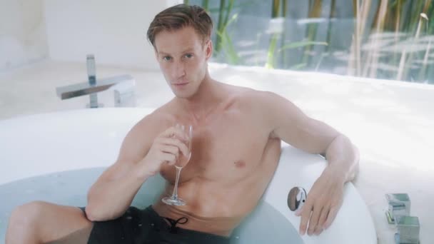 Handsome man drinks champagne sitting in modern bathtub — Stockvideo