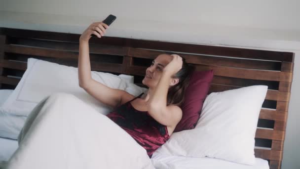 Красивая брюнетка девушка в бархатной пижаме делает селфи на кровати — стоковое видео