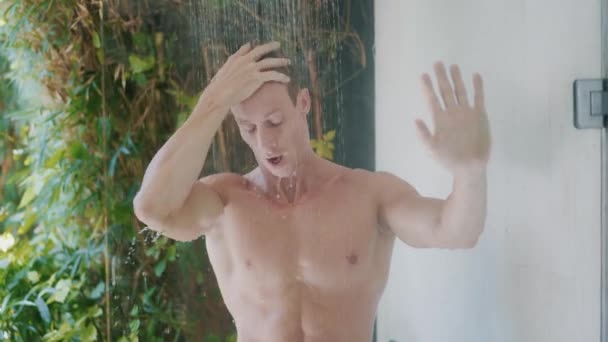 Joven con cuerpo fuerte toma refrescante ducha en casa — Vídeos de Stock