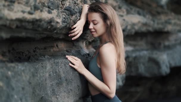 Girl poses for camera leaning on cliff and adjusting hair — Stockvideo