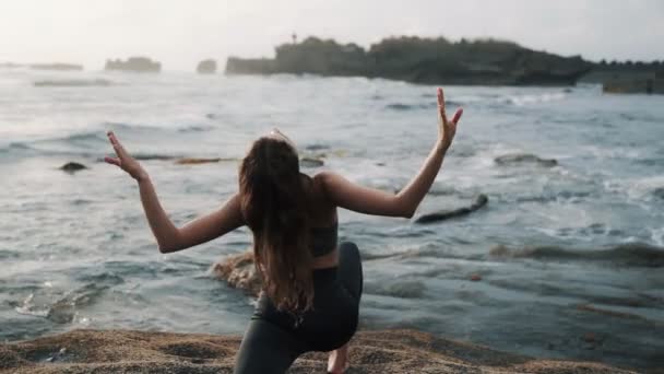 Girl does stretching standing on stone against waving ocean — Stockvideo