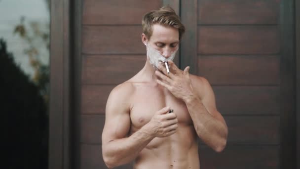 Hombre torso desnudo con espuma de afeitar en la cara fuma cigarrillo — Vídeos de Stock