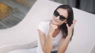 brunette girl wearing sunglasses smiles on couch at resort