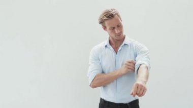 guy with fair hair rolls up sleeves and fixes collar