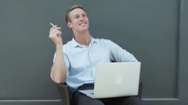guy with fair hair smokes cigarette looks at laptop screen