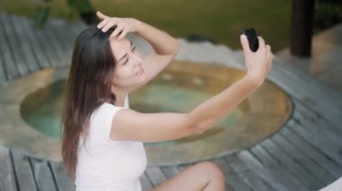 Zarif bayan tropik tatil köyünde havuz kenarında selfie çekiyor.